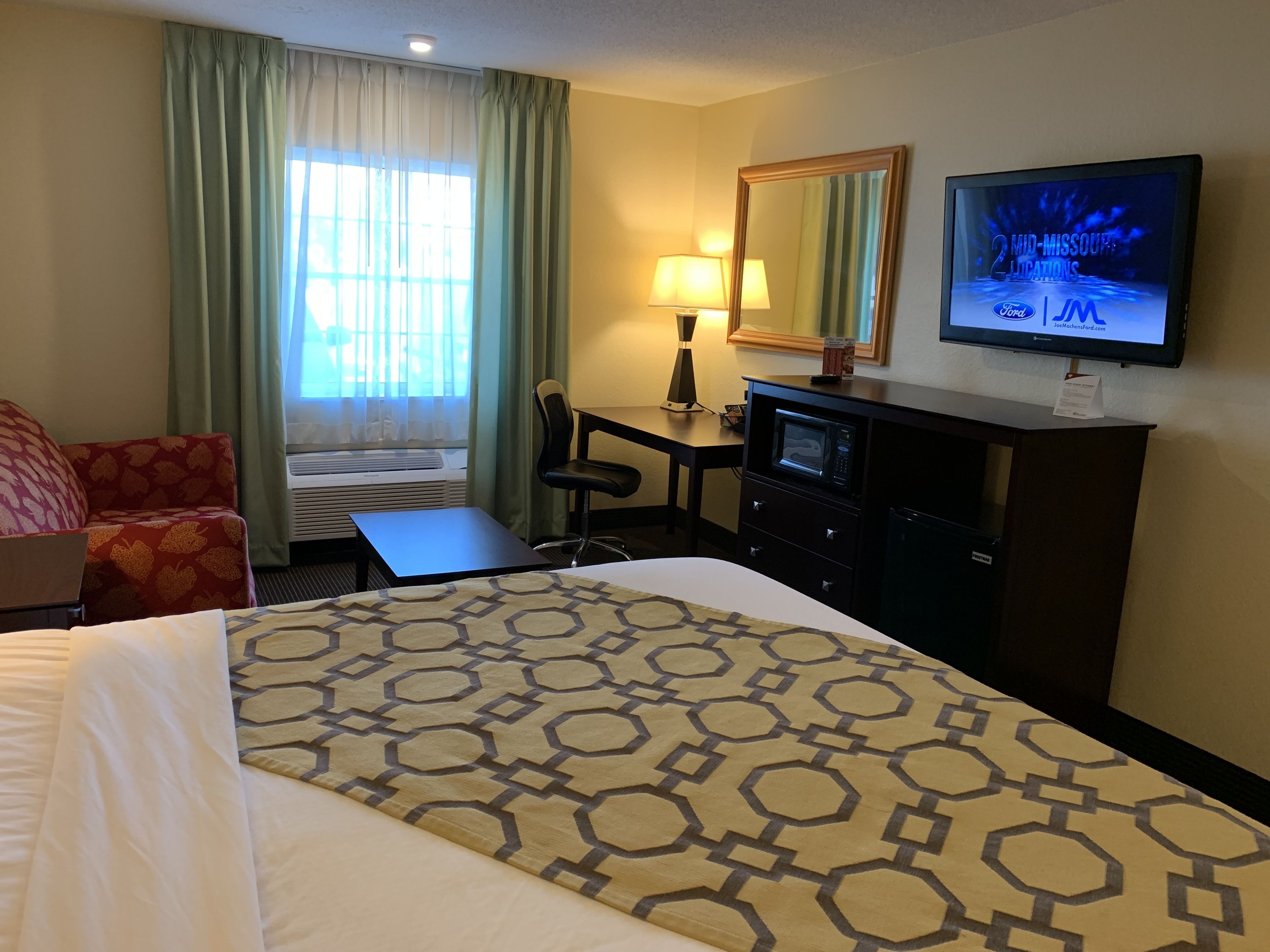 Een hotelkamer met een bed, een bureau, een stoel, een televisie en een raam met gordijnen.
