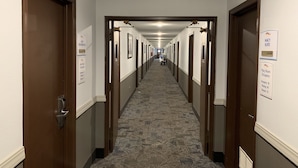 Een hotelgang met deuren aan beide kanten, borden met aanduiding van kamertypes en voorzieningen, en een vloerbedekking.