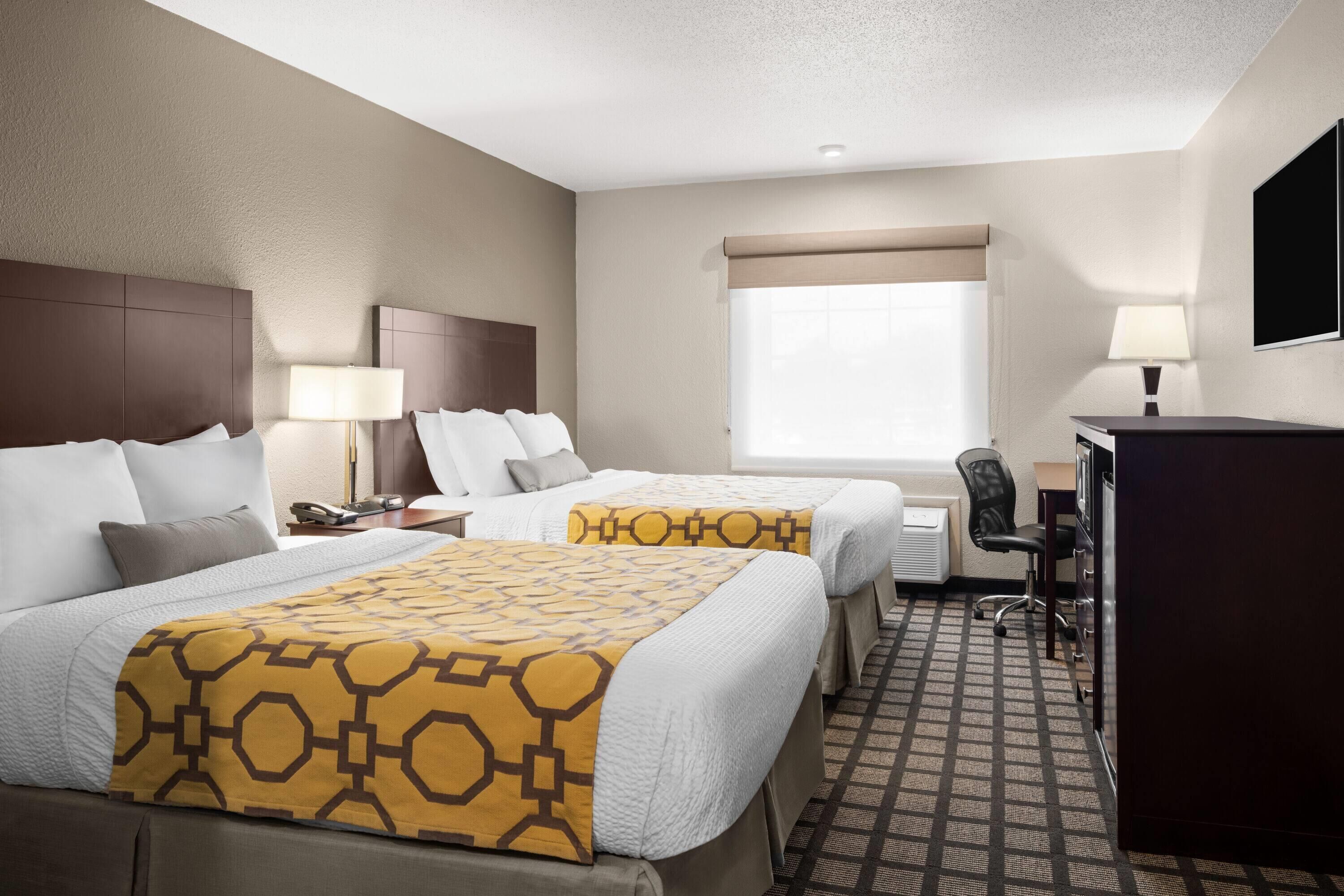 A hotel room with two beds, a desk, a chair, and a television.