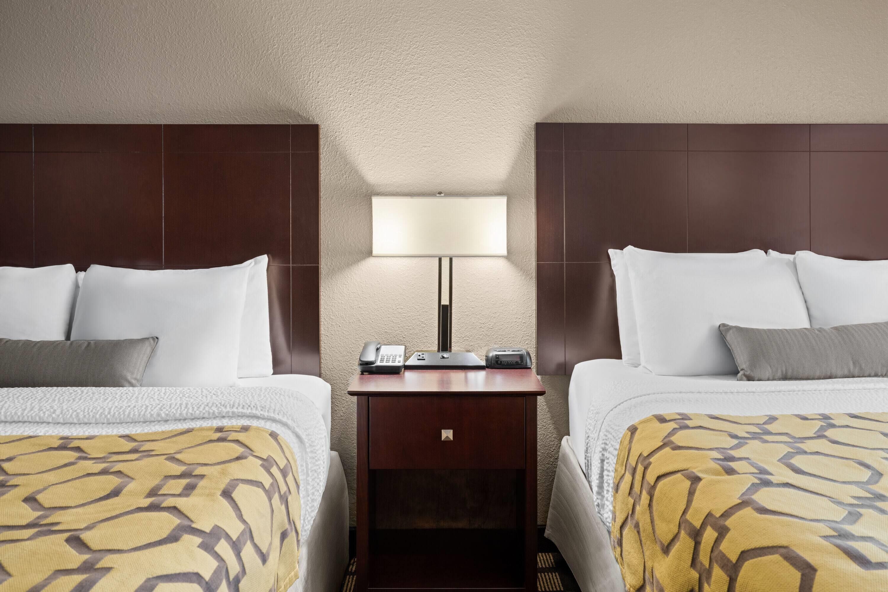 Quarto de hotel com duas camas, uma mesa de cabeceira com abajur e um telefone.