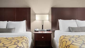 Quarto de hotel com duas camas, uma mesa de cabeceira com abajur e um telefone.