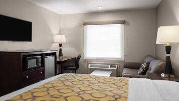Ein Hotelzimmer mit Bett, Schreibtisch mit Stuhl, Flachbildfernseher, Mikrowelle, Kühlschrank, Fenster mit Jalousien und einer Lampe.