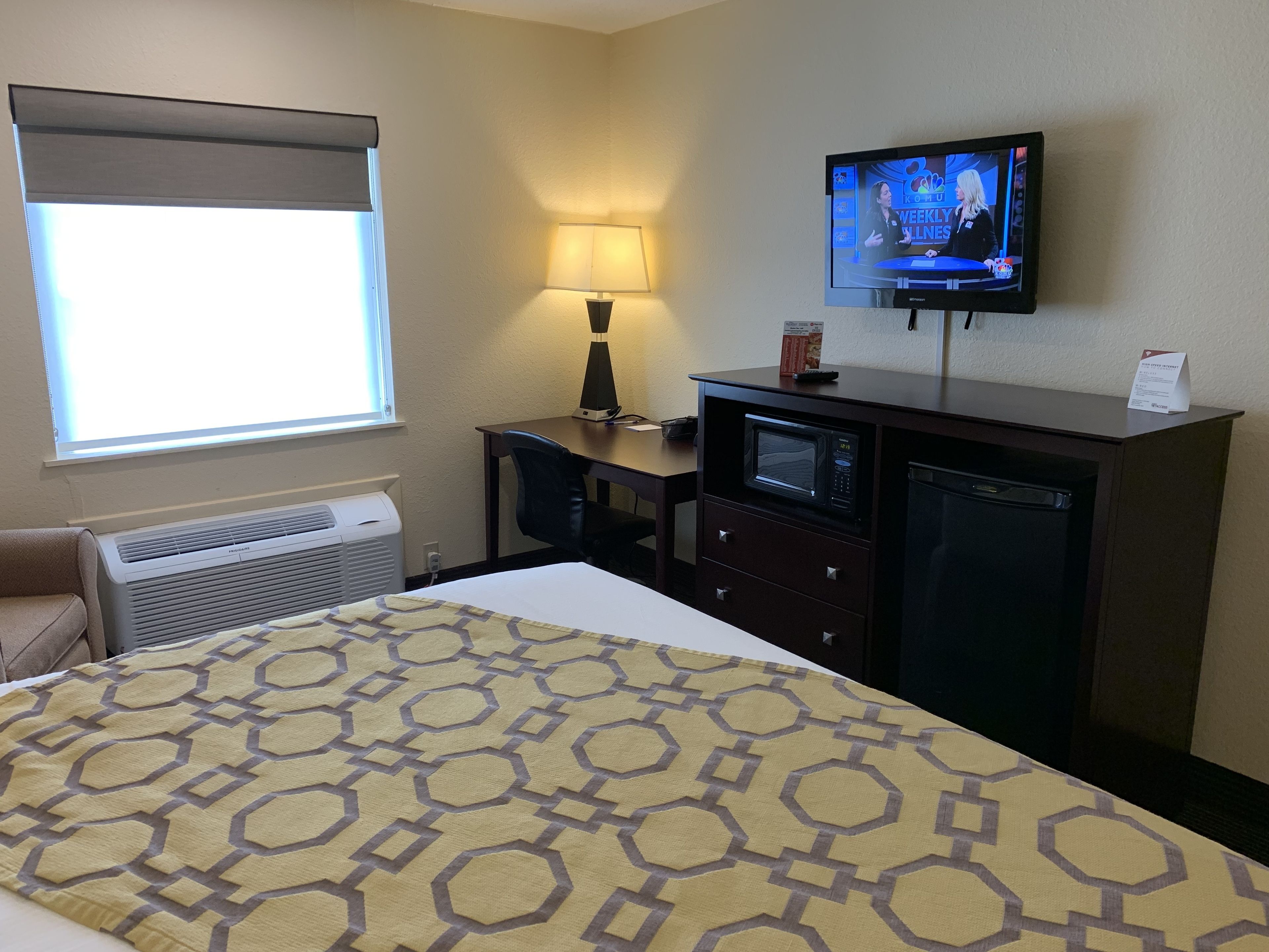 A hotel room with a bed, a desk, a television, a lamp, and a microwave.