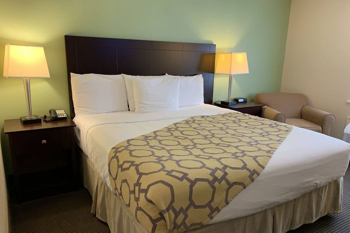 Ein Hotelzimmer mit einem großen Bett, zwei Nachttischlampen, einem Sessel und einem Nachttisch mit Telefon.