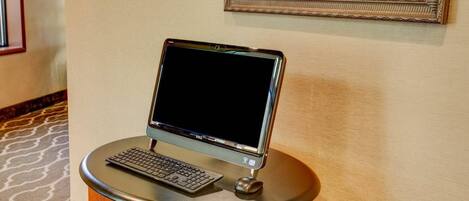 Un ordinateur de bureau est posé sur une table en bois dans le hall d’un hôtel, et un tableau encadré est accroché au mur.