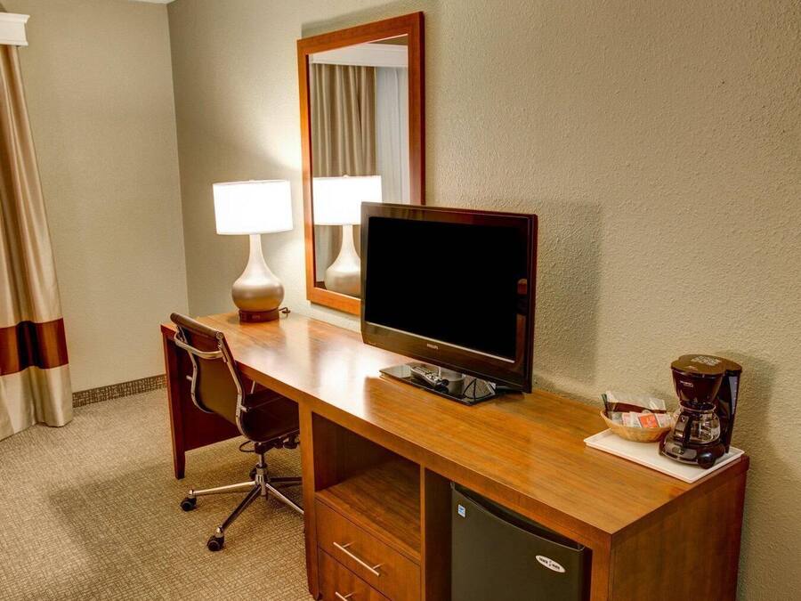 Habitació d'hotel amb escriptori de fusta, televisió, cafetera, cadira i nevera.
