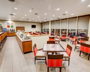 A spacious dining area with multiple tables and chairs, a counter with food service equipment, and a television mounted on the wall.