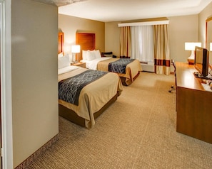 A hotel room with two beds, a desk, a chair, a lamp, a TV, and a window with curtains.