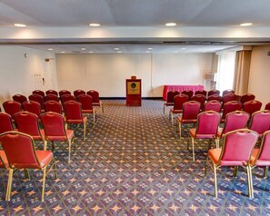 A conference room with rows of red chairs, a podium, and a patterned carpet.