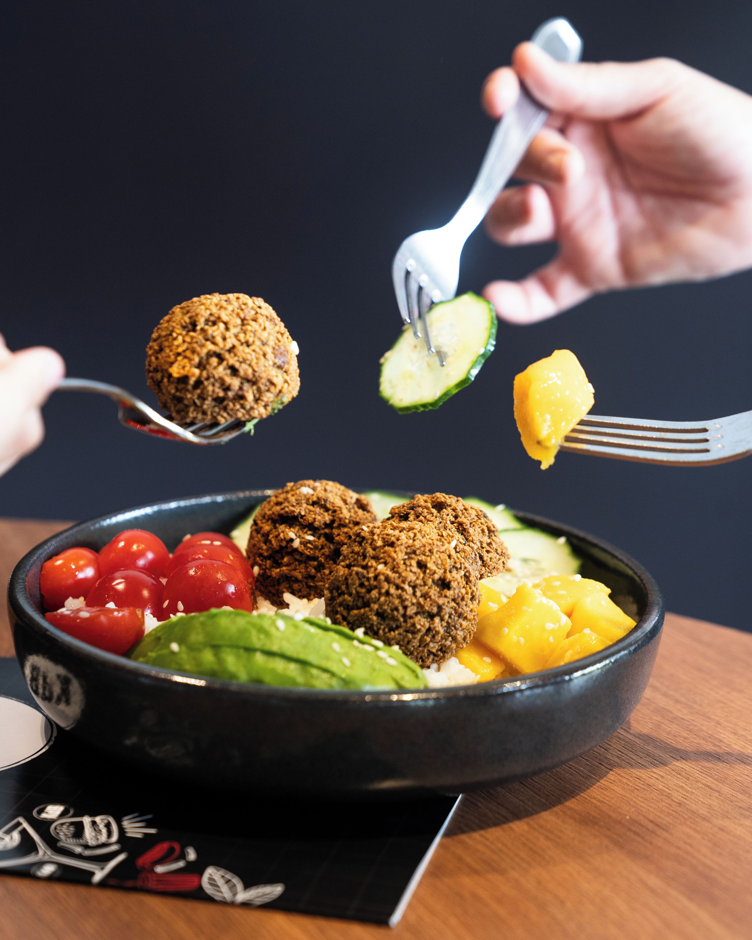 Un bol de menjar amb boletes de falafel, tomàquets cherries, advocat i trossos de mango.