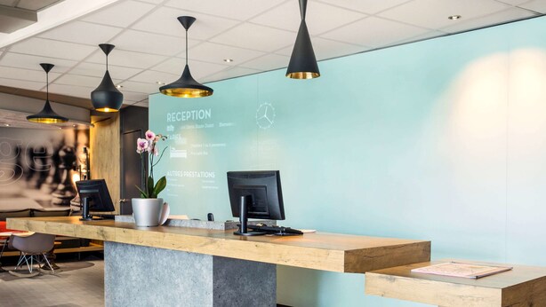 Un mostrador de recepción de diseño moderno, con una pared azul claro, una encimera de madera e iluminación colgante negra.