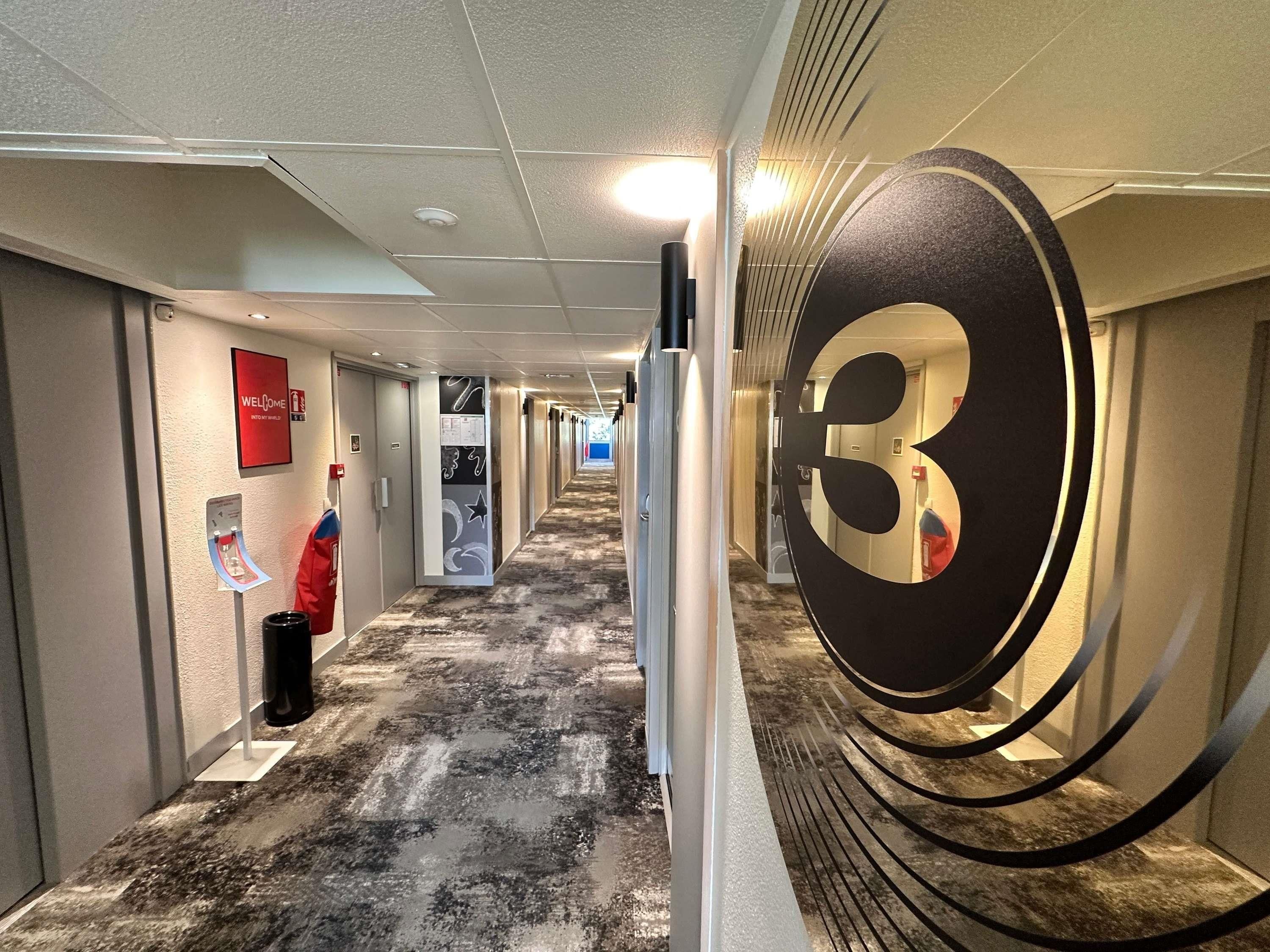 A hotel corridor with a large number '3' sign, a welcome sign, and a fire extinguisher.