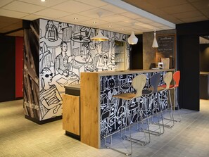Una zona de bar con un mural en blanco y negro, una barra de madera y sillas de metal.