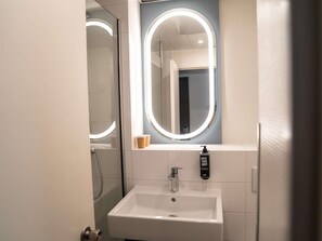 Un baño con lavamanos blanco, un espejo con luz circular y dispensador de jabón.