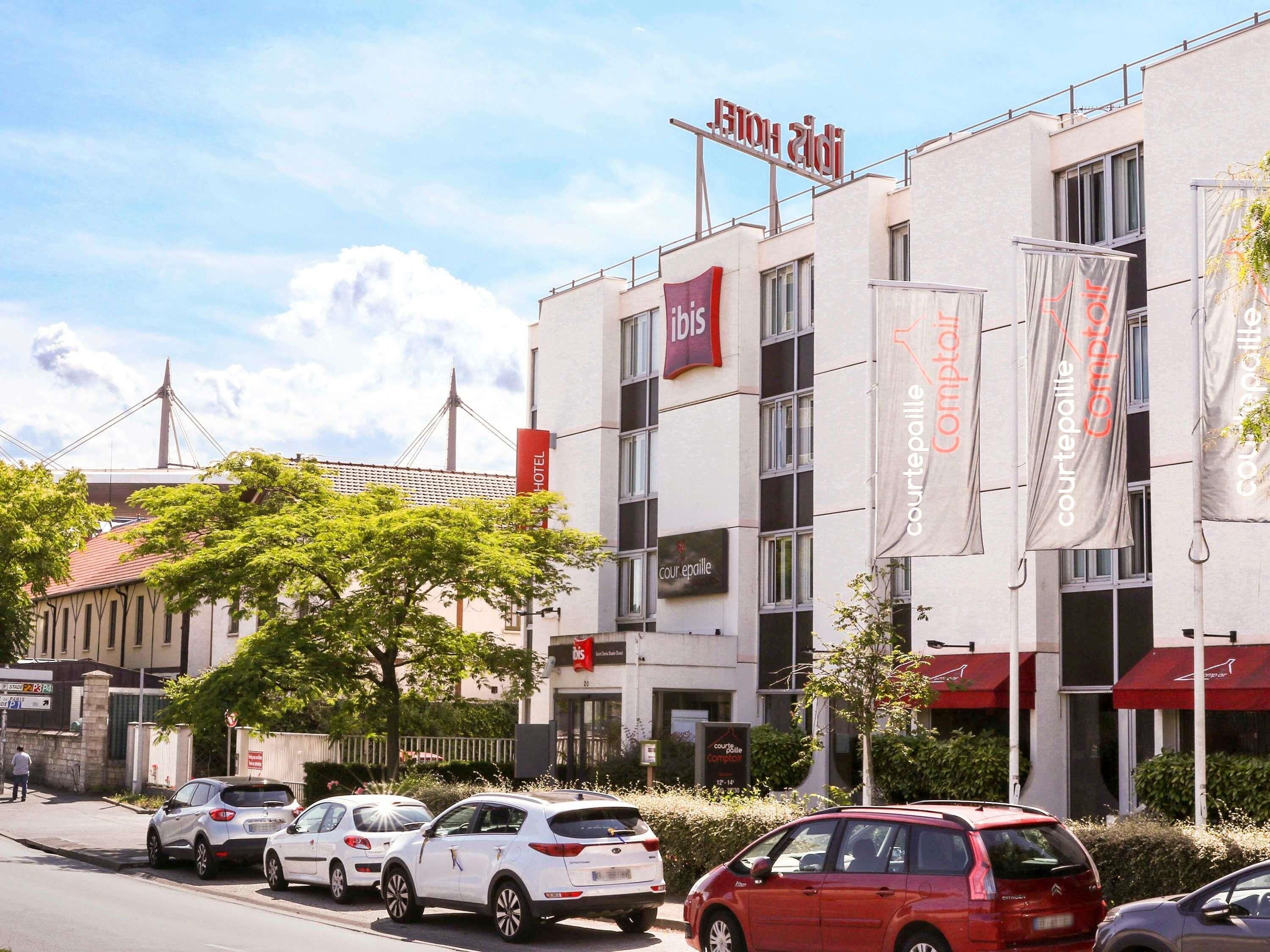 Un bâtiment d’hôtel avec une enseigne indiquant « HÔTEL ibis » et plusieurs banderoles faisant la publicité de « Courtepaille Comptoir ».