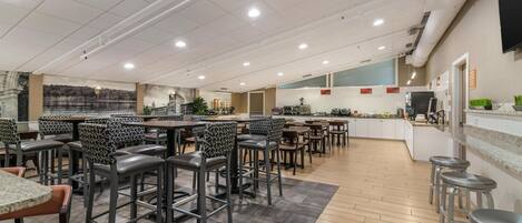 A spacious restaurant with high ceilings, modern lighting, and a variety of seating options including bar stools and tables.