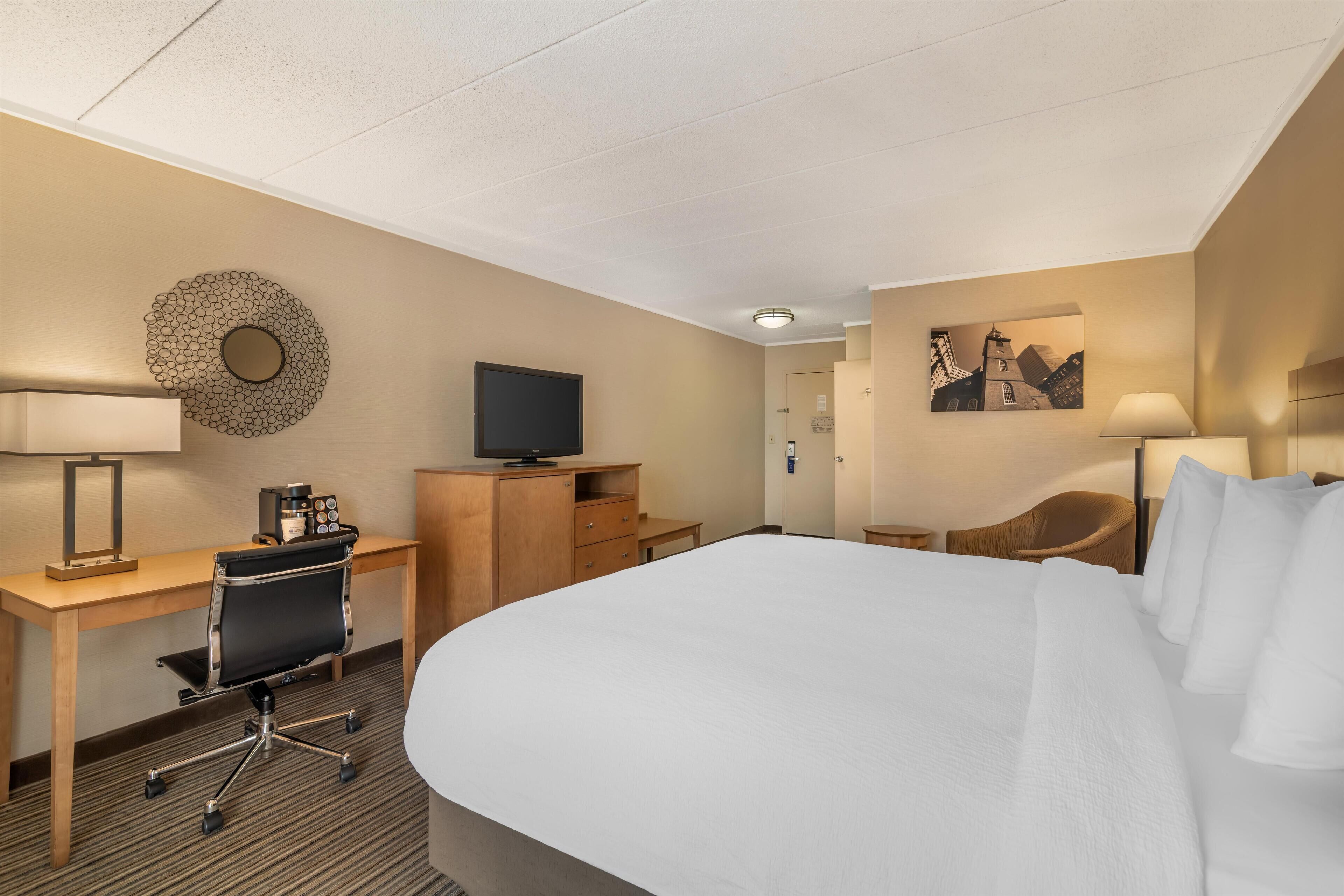 Une chambre d’hôtel avec un grand lit, un bureau avec une chaise, une télévision et une machine à café.