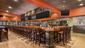 A bar area with a long counter, multiple bar stools, and a variety of bottles and glasses. - Best Western Plus Waltham Boston (Waltham)