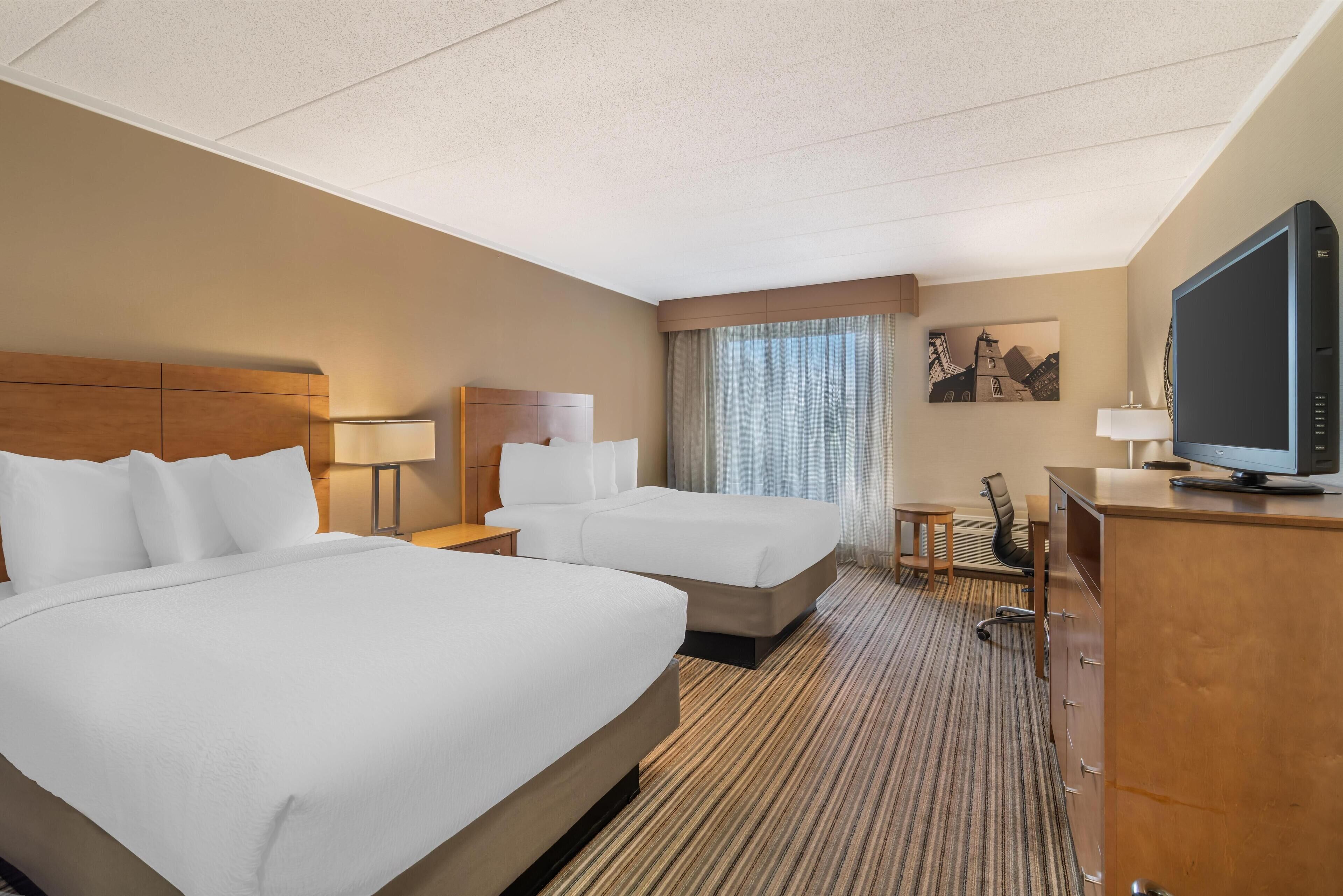 Ein Hotelzimmer mit zwei Betten, einem Schreibtisch, einem Fernseher und einem Bild an der Wand.
