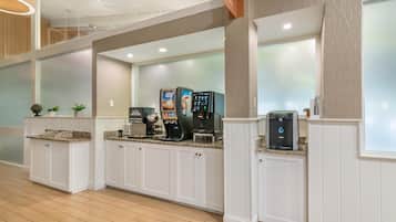 A hotel lobby with a coffee station, seating area, and a large window.