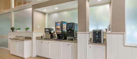 Un vestíbulo de hotel con una estación de café, zona de estar y un gran ventanal.