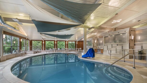 An indoor swimming pool with clear water, surrounded by windows and covered by large, neutral-colored canopies. - Best Western Plus Waltham Boston (Waltham)