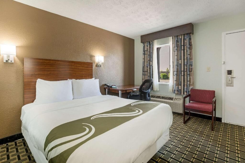 A hotel room with a bed, a desk, a chair, and a window with curtains.
