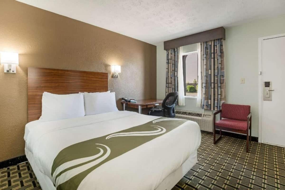 A hotel room with a bed, a desk, a chair, and a window with curtains.