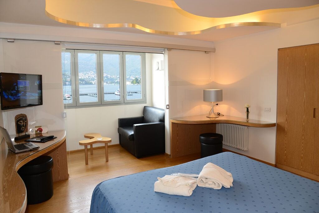 A hotel room with a bed, a desk, a chair, a TV, a window with a view, and a lamp.