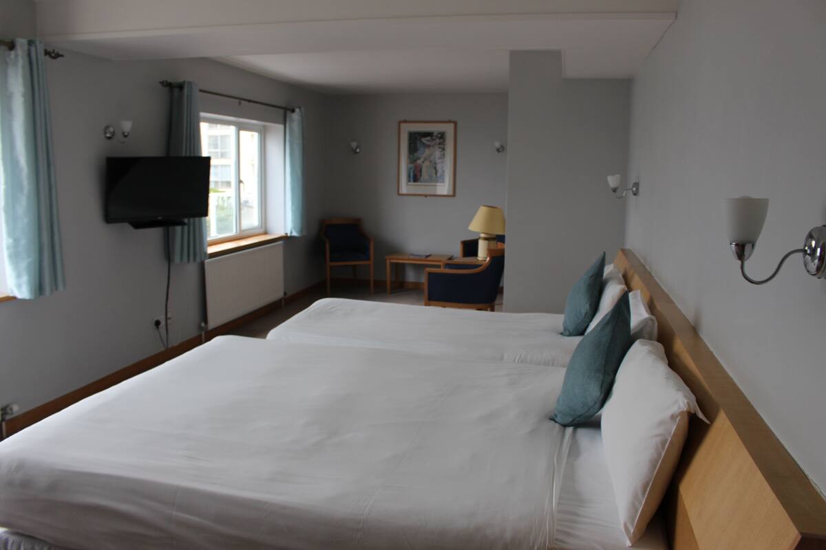 A hotel room with two beds, a desk, a chair, a television, and a window with curtains.