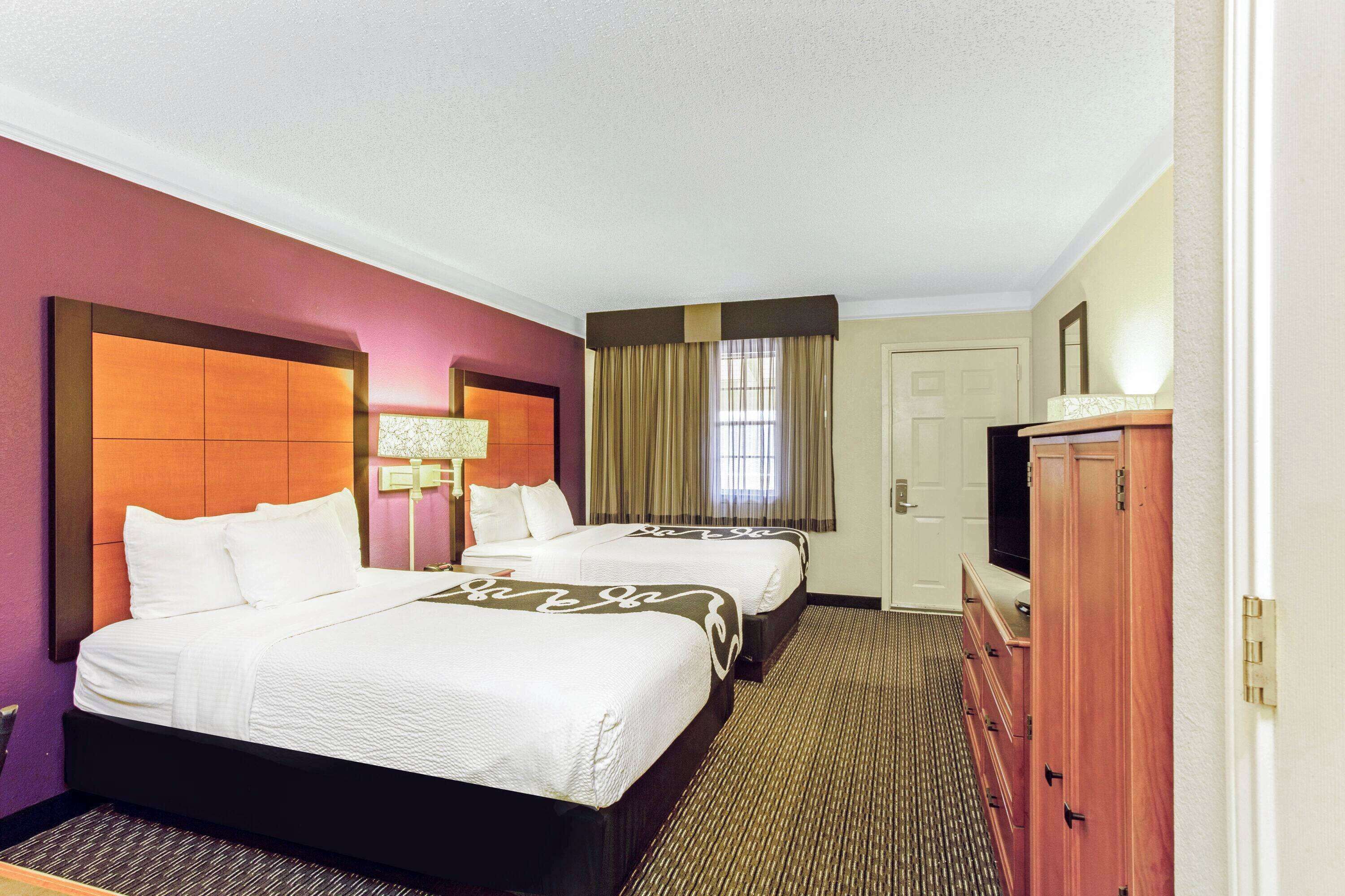 Habitación de hotel con dos camas, un aparador, televisor y ventana con cortinas.