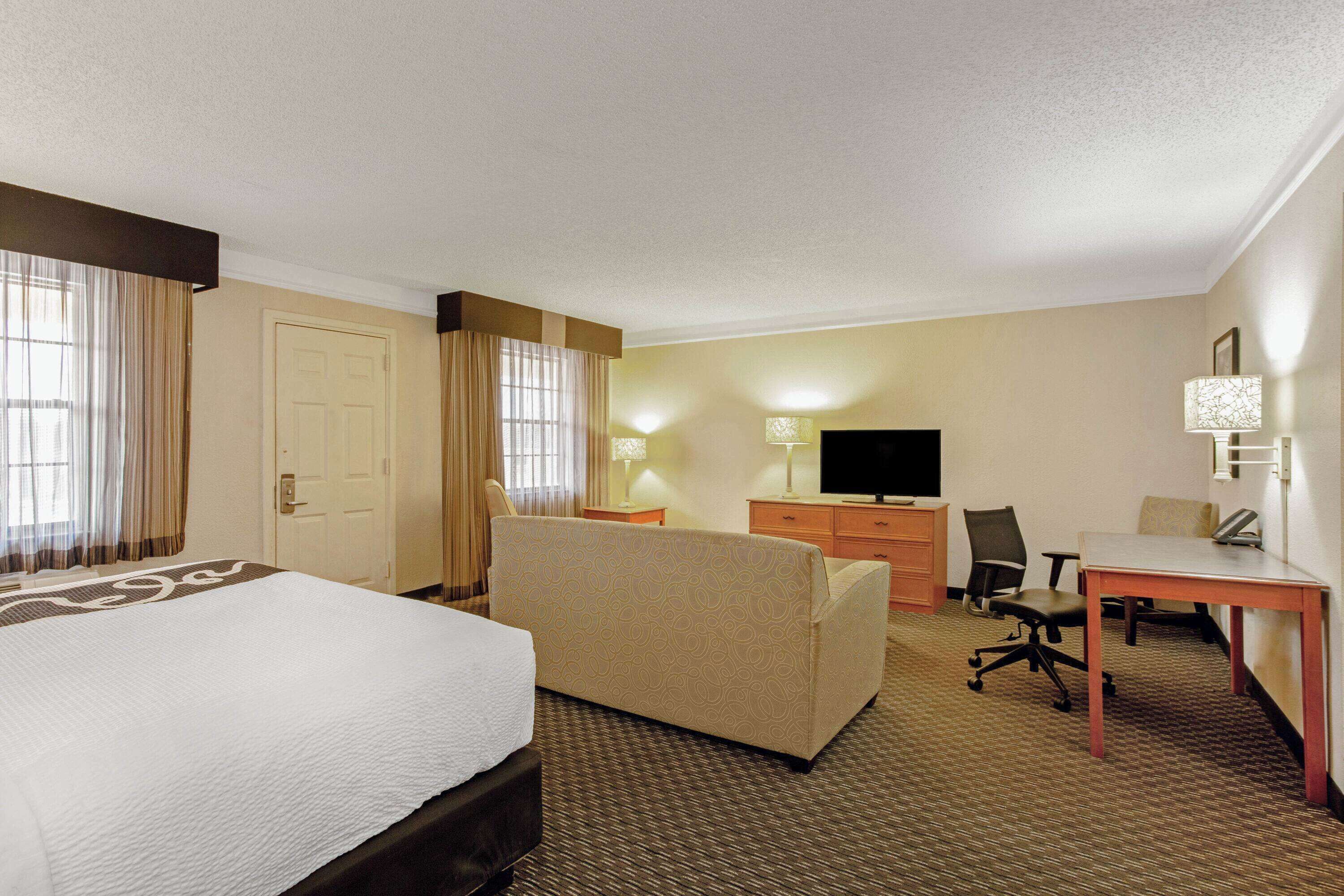A hotel room with a large bed, a sofa, a desk, a TV, and a lamp.