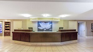 Een receptiegedeelte met een groot bloemenkunstwerk, een gebogen receptiebalie en een betegelde vloer.