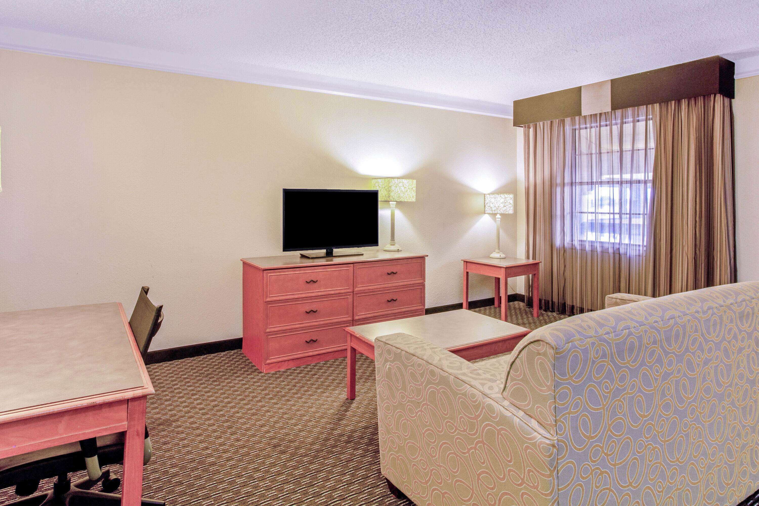 A hotel room with a bed, a desk, a chair, a television, a dresser, and a window with curtains.
