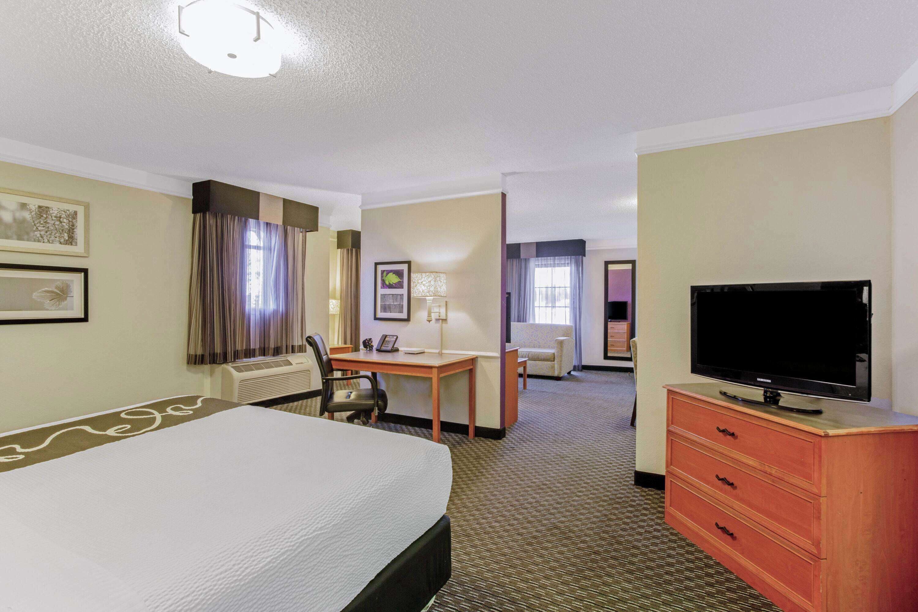 A hotel room with a bed, a desk, a chair, a television, and a dresser.