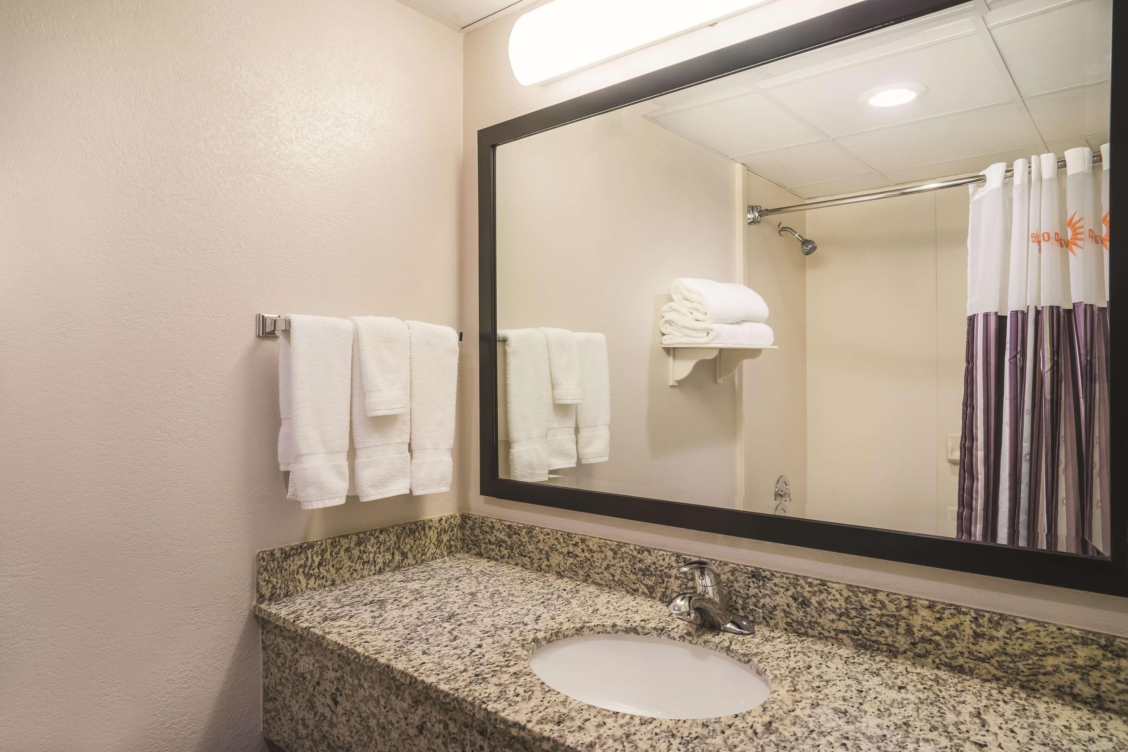 A bathroom with a granite countertop sink, a large mirror, and a shower with a striped curtain.