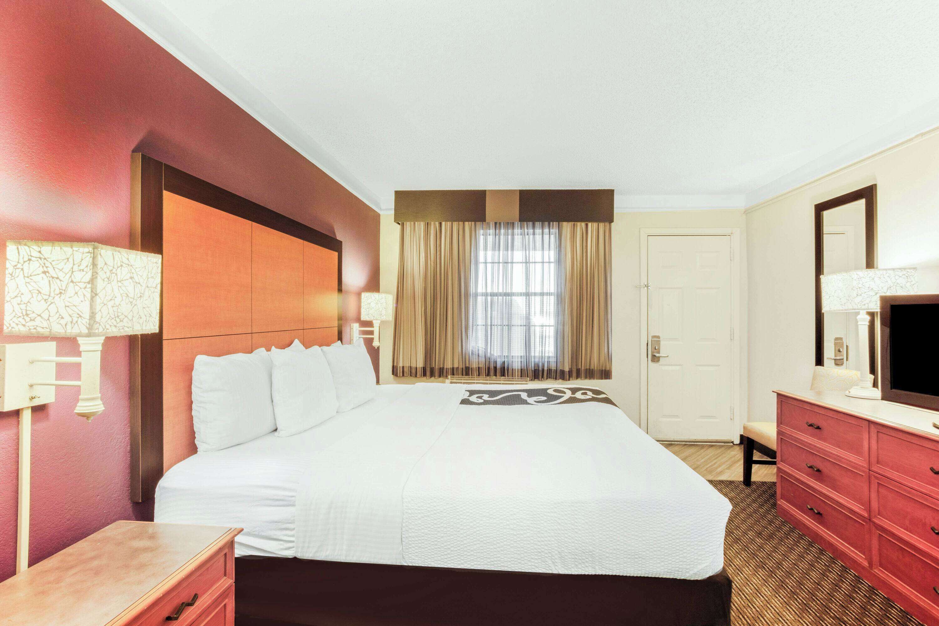 A hotel room with a large bed, a dresser, a television, and a window with curtains.