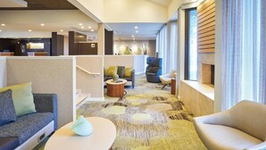 A modern hotel lobby with a reception desk, seating areas, and a patterned carpet.