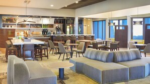 A modern hotel lobby with a bar area, seating arrangements, and a view of the outdoors.