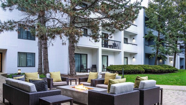 An outdoor seating area with wicker furniture, a fire pit, and a view of a modern building with balconies.