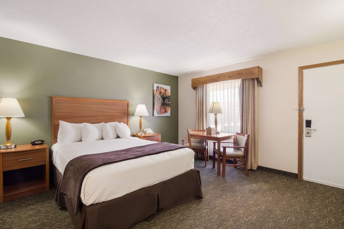 A hotel room with a large bed, two bedside tables with lamps, a desk with a chair, and a window with curtains.
