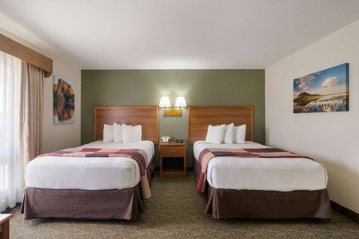 A hotel room with two beds, a nightstand, and a painting on the wall.