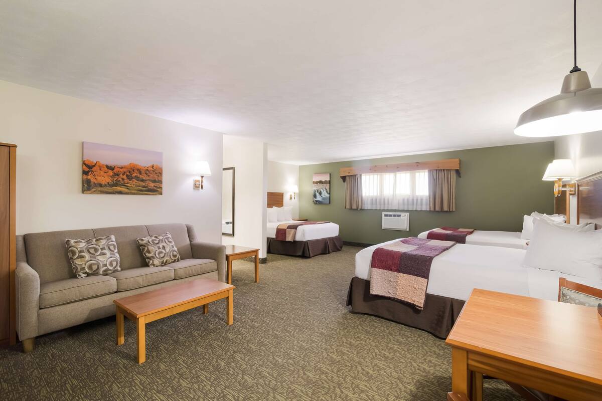 A hotel room with a sofa, two beds, a wooden table, and a painting on the wall.