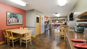 Un restaurante con comedor que incluye una mesa y sillas de madera, una zona de cocina con mostrador y una vitrina con alimentos.