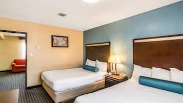 Una habitación de hotel con dos camas, una mesita de noche con lámpara, un cuadro enmarcado en la pared y una silla roja en la habitación contigua.