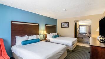 A hotel room with two beds, a desk, a chair, and a bathroom visible through an open door.