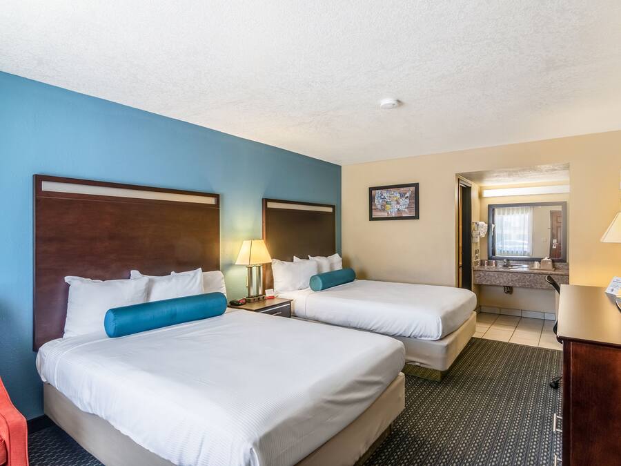 A hotel room with two beds, a desk, a chair, and a bathroom visible through an open door.