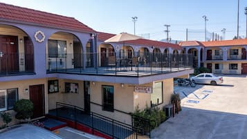 Een motel met een gebouw van twee verdiepingen, een overdekte buitenzitplaats en een parkeerplaats met een motor.
