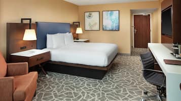 A hotel room with a bed, two bedside tables with lamps, a desk with a chair, and a bathroom door.