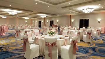 A banquet hall with round tables, white chairs with pink sashes, and a carpeted floor.